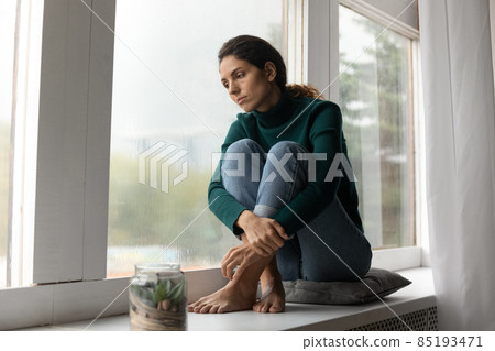 Sad hispanic lady sit barefoot on windowsill feel absent minded Sad hispanic lady sit barefoot on windowsill feel absent minded 85193471