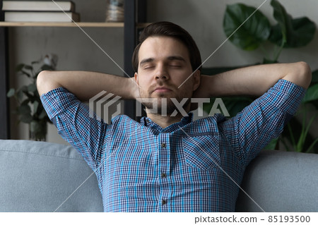 Man put hands behind head resting leaned on cozy sofa Man put hands behind head resting leaned on cozy sofa 85193500