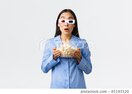 Home leisure, sleepover and slumber party concept. Astounded and impressed asian girl in pajamas, watching thriller, holding bowl of popcorn and wear 3d glasses, stare at tv in awe 85193520