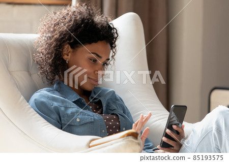 Attractive calm African woman relaxing on cozy armchair with smartphone 85193575