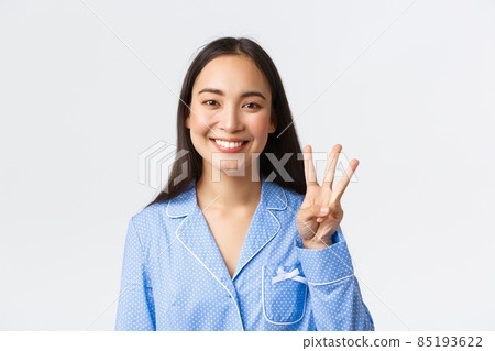 Close-up shot of happy attractive asian woman in blue pyjama showing three fingers and smiling white teeth, explain main rules or making order, standing white background delighted 85193622
