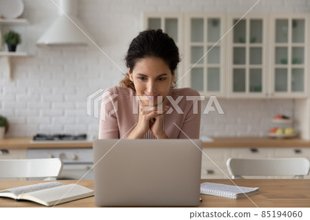Smiling woman looking at laptop screen, working online in kitchen 85194060