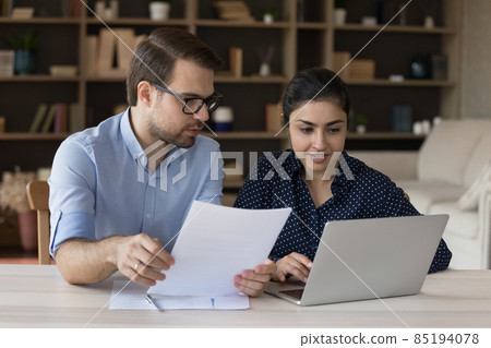 Two diverse coworker employees sharing laptop, discussing paper report 85194078
