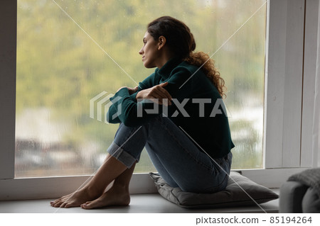 Pensive Latino woman relax at home looking in window Pensive Latino woman relax at home looking in window 85194264