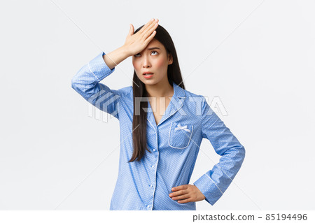 Annoyed asian girl in blue pajamas rolling eyes bothered and facepalm, punch forehead with arm from irritation, listening something lame, standing white background 85194496
