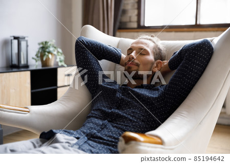 Calm guy relaxing in pale comfortable armchair at home 85194642
