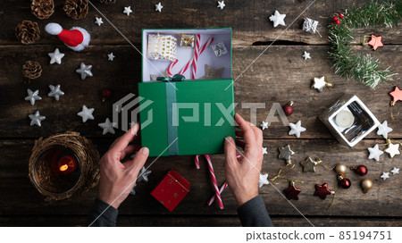 Opening or closing a green holiday gift box on rustic wooden desk full of christmas ornaments 85194751