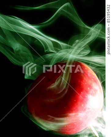 Green smoke envelops a round red apple on a black background Green smoke envelops a round red apple on a black background 85195432