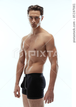 Half-length portrait of young handsome shirtless sportive man wearing black boxer-briefs standing isolated on white background. 85197081