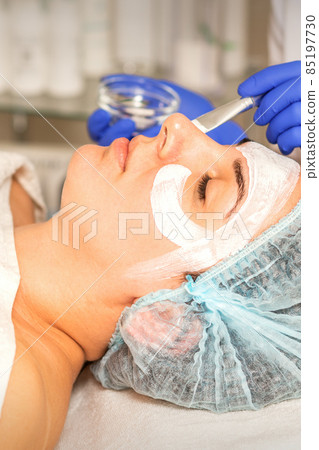 Face peeling at the beautician. Facial treatment. The beautician applies a cleansing face mask to the female patient. 85197730