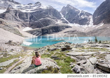 Female hiker sitting on the bank of turquoise glacier lake in beautiful alpine environment 85199342