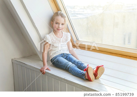 Little cute sweet smiling girl in jeans and white T-shirt sitting on the window sill in bright light living room at home and thinking Childhood, schoolchildren, youth, relax concept Little cute sweet smiling girl in jeans and white T-shirt sitting on the window sill in bright light living room at home and thinking Childhood, schoolchildren, youth, relax concept 85199739