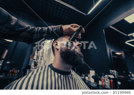 Barber works with a beard clipper. Hipster client getting haircut. Barber works with a beard clipper. Hipster client getting haircut. 85199966