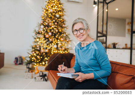 Grandma sits on the couch writing something in a note Grandma sits on the couch writing something in a note 85200083
