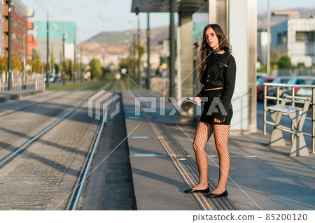 young woman waiting for the tram at the stop young woman waiting for the tram at the stop 85200120