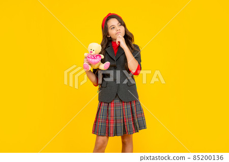 pondering teen girl in uniform holding toy on yellow background, school 85200136