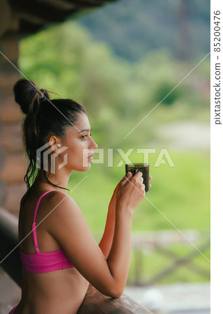 Side view portrait of a happy woman in pink swimsuit with coffee cup Side view portrait of a happy woman in pink swimsuit with coffee cup 85200476