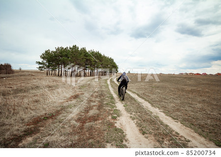 A man on a bicycle rides on a road in a rural area. 85200734