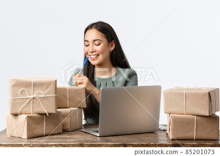 Small business owners, startup and e-commerce concept. Smiling successful asian businesswoman open online store, writing shipping info on boxes with client orders, managing delivery, use laptop Small business owners, startup and e-commerce concept. Smiling successful asian businesswoman open online store, writing shipping info on boxes with client orders, managing delivery, use laptop 85201073