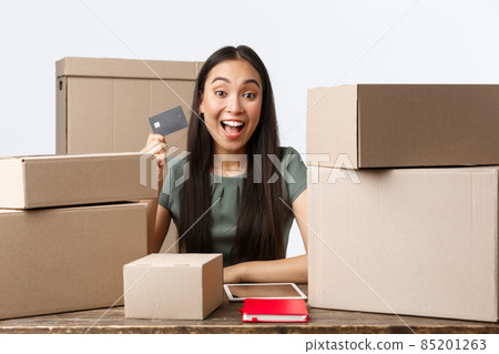 Small business owners, startup and e-commerce concept. Happy asian businesswoman selling online, showing credit card and smiling, except payments on bank account, process orders, packing in boxes 85201263