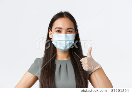Small business owners, covid-19, preventing virus measures concept. Close-up of confident smiling asian woman in medical mask and gloves, show thumbs-up, provide safety during work in office Small business owners, covid-19, preventing virus measures concept. Close-up of confident smiling asian woman in medical mask and gloves, show thumbs-up, provide safety during work in office 85201264