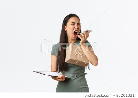 Pissed-off angry asian female business owner, shop manager yelling at rude client over phone, holding box with items for shipping to customers and shouting in smartphone aggressive, losing temper 85201321