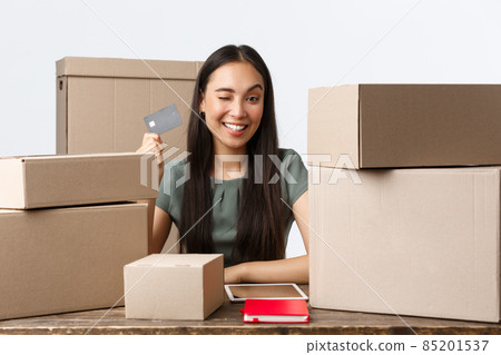 Small business owners, startup and e-commerce concept. Successful asian businesswoman showing credit card, except contactless payment while selling products online, wink cheeky and smiling Small business owners, startup and e-commerce concept. Successful asian businesswoman showing credit card, except contactless payment while selling products online, wink cheeky and smiling 85201537