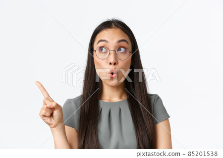 Impressed attractive asian woman checking-out banner with special offer, shop discounts. Female in glasses pointing finger and looking upper left corner with amazed, surprised expression 85201538