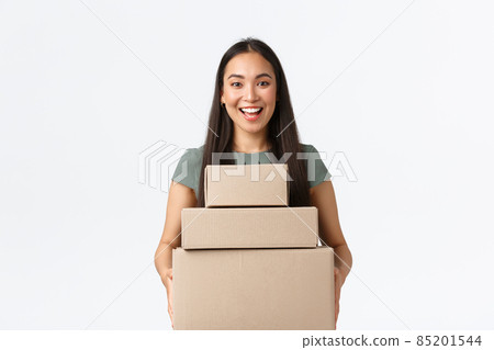 Small business owners, startup and work from home concept. Cheerful asian female store manager carry boxes with clients orders at post office, making delivery of purchased iteam, white background 85201544