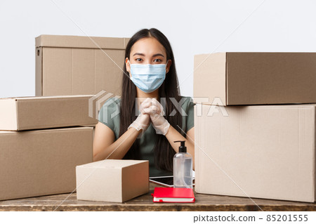Small business owners, e-commerce and covid-19 preventing virus concept. Successful asian businesswoman care for customers safety, using medical mask and gloves before processing online order Small business owners, e-commerce and covid-19 preventing virus concept. Successful asian businesswoman care for customers safety, using medical mask and gloves before processing online order 85201555