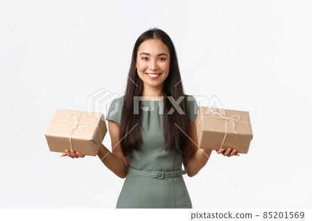 Small business owners, startup and work from home concept. Smiling asian female shop owner, packing items for shipping, holding two packages, carry to delivery company, sending product to customers 85201569