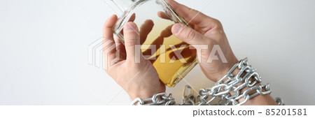 Male hands tied with chain and hold bottle of alcohol closeup Male hands tied with chain and hold bottle of alcohol closeup 85201581