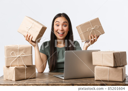 Small business owners, startup and e-commerce concept. Smiling asian businesswoman working from home managing online store via laptop, packing parcels for clients, checking info for shipping Small business owners, startup and e-commerce concept. Smiling asian businesswoman working from home managing online store via laptop, packing parcels for clients, checking info for shipping 85201604