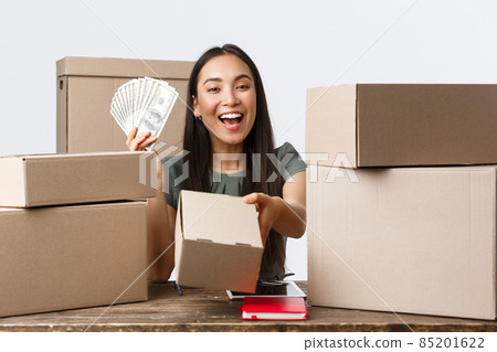 Small business owners, startup and e-commerce concept. Smiling asian woman showing money and giving box with order, selling online, earn cash for internet store, shipping handmade products 85201622