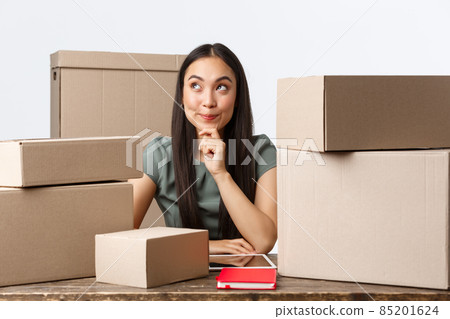 Small business owners, startup and e-commerce concept. Thoughtful creative asian woman open internet store, thinking how make profit, better income, sitting near lots of boxes ready for shipping Small business owners, startup and e-commerce concept. Thoughtful creative asian woman open internet store, thinking how make profit, better income, sitting near lots of boxes ready for shipping 85201624