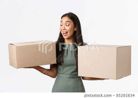 Small business owners, startup and work from home concept. Amazed happy asian woman holding two boxes with her orders, looking cheerful and pleased, collect parcels from post-office Small business owners, startup and work from home concept. Amazed happy asian woman holding two boxes with her orders, looking cheerful and pleased, collect parcels from post-office 85201634