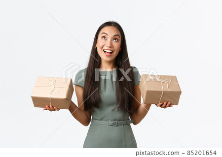 Happy dreamy asian female entrepreneur, small business owner packing items herself, sending packages to customers who ordered products online store, standing white background and looking up Happy dreamy asian female entrepreneur, small business owner packing items herself, sending packages to customers who ordered products online store, standing white background and looking up 85201654