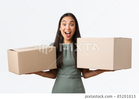 Small business owners, startup and work from home concept. Excited happy asian woman holding two boxes with her orders from online shop, receive delivery and smiling amazed, white background 85201813