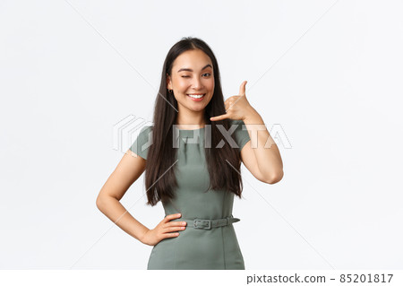 Small business owners, startup and work from home concept. Smiling cheeky asian woman winking and smiling, encourage clients give her call, shop assistant answering client questiones via phone 85201817
