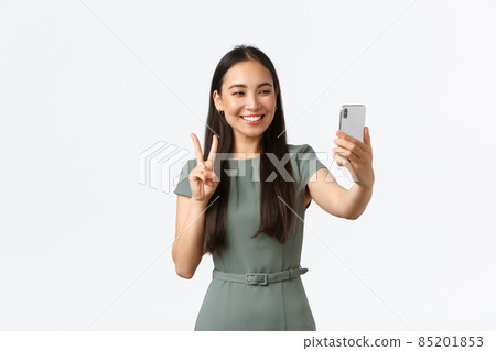 Small business owners, women entrepreneurs concept. Gorgeous feminine asian female blogger taking selfie on smartphone, posing and looking at mobile phone camera with peace sign 85201853