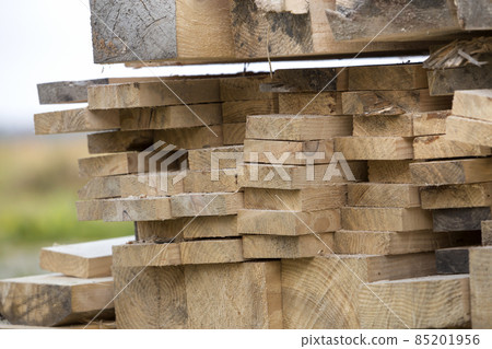 Close-up of piled stack of natural brown uneven rough wooden boards lit by bright sun. Industrial timber for carpentry, building, repairing and furniture, lumber material for construction. Close-up of piled stack of natural brown uneven rough wooden boards lit by bright sun. Industrial timber for carpentry, building, repairing and furniture, lumber material for construction. 85201956