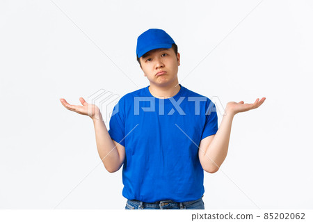 Portrait of shrugging and clueless asian delivery man in blue uniform raising hands sideways unaware. Courier dont know anything, standing sad and gloomy without answer, white background Portrait of shrugging and clueless asian delivery man in blue uniform raising hands sideways unaware. Courier dont know anything, standing sad and gloomy without answer, white background 85202062