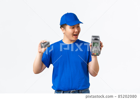 Contactless shopping, payment and employees concept. Amazed asian courier, delivery man in blue uniform looking at POS terminal and holding credit card, standing white background Contactless shopping, payment and employees concept. Amazed asian courier, delivery man in blue uniform looking at POS terminal and holding credit card, standing white background 85202080