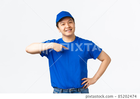 Proud confident smiling asian courier in blue uniform pointing at himself and looking pleased, assure parcels are saved with fast home delivery, ensure and guarantee best service, white background 85202474
