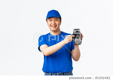 Contactless shopping, payment and employees concept. Smiling friendly-looking asian courier, delivery man in blue uniform show how to pay, press credit card to POS terminal, white background Contactless shopping, payment and employees concept. Smiling friendly-looking asian courier, delivery man in blue uniform show how to pay, press credit card to POS terminal, white background 85202482