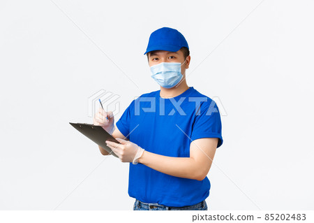 Contactless delivery, covid-19 shipping, preventing virus concept. Smiling asian male courier in medical mask and blue uniform, manager confirm shipment info, inspecting, writing on clipboard 85202483