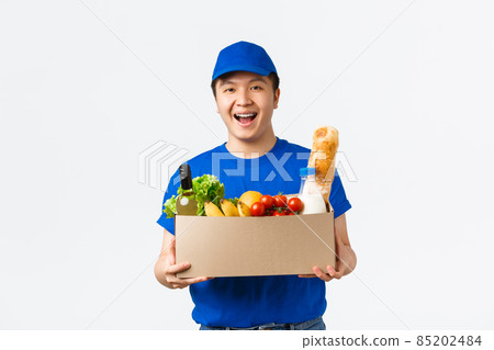 Online shopping, food delivery and shipment concept. Cheerful smiling young asian courier in blue uniform handing box with groceries, bring order to customer home, white background Online shopping, food delivery and shipment concept. Cheerful smiling young asian courier in blue uniform handing box with groceries, bring order to customer home, white background 85202484