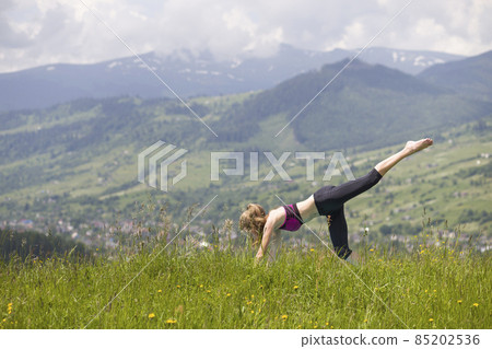 Attractive slim young woman doing yoga exercises outdoors on copy space background of mountains. Attractive slim young woman doing yoga exercises outdoors on copy space background of mountains. 85202536