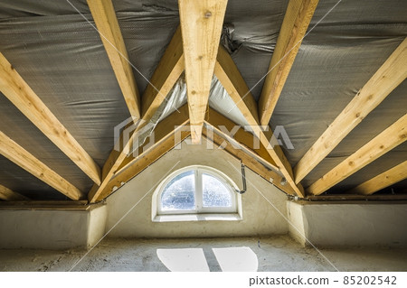 Attic of a building with wooden beams of a roof structure and a small window. 85202542
