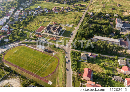 Aerial view of a football field on a stadium covered with green grass in rural town area. Aerial view of a football field on a stadium covered with green grass in rural town area. 85202643